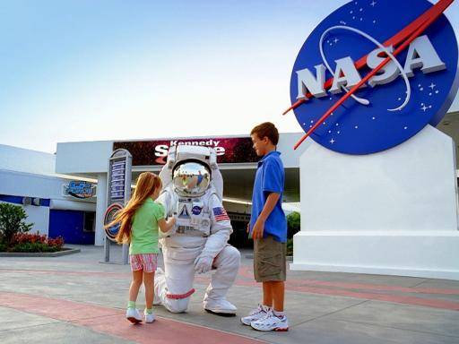 astronaut kneeling down to two children outside space centre 