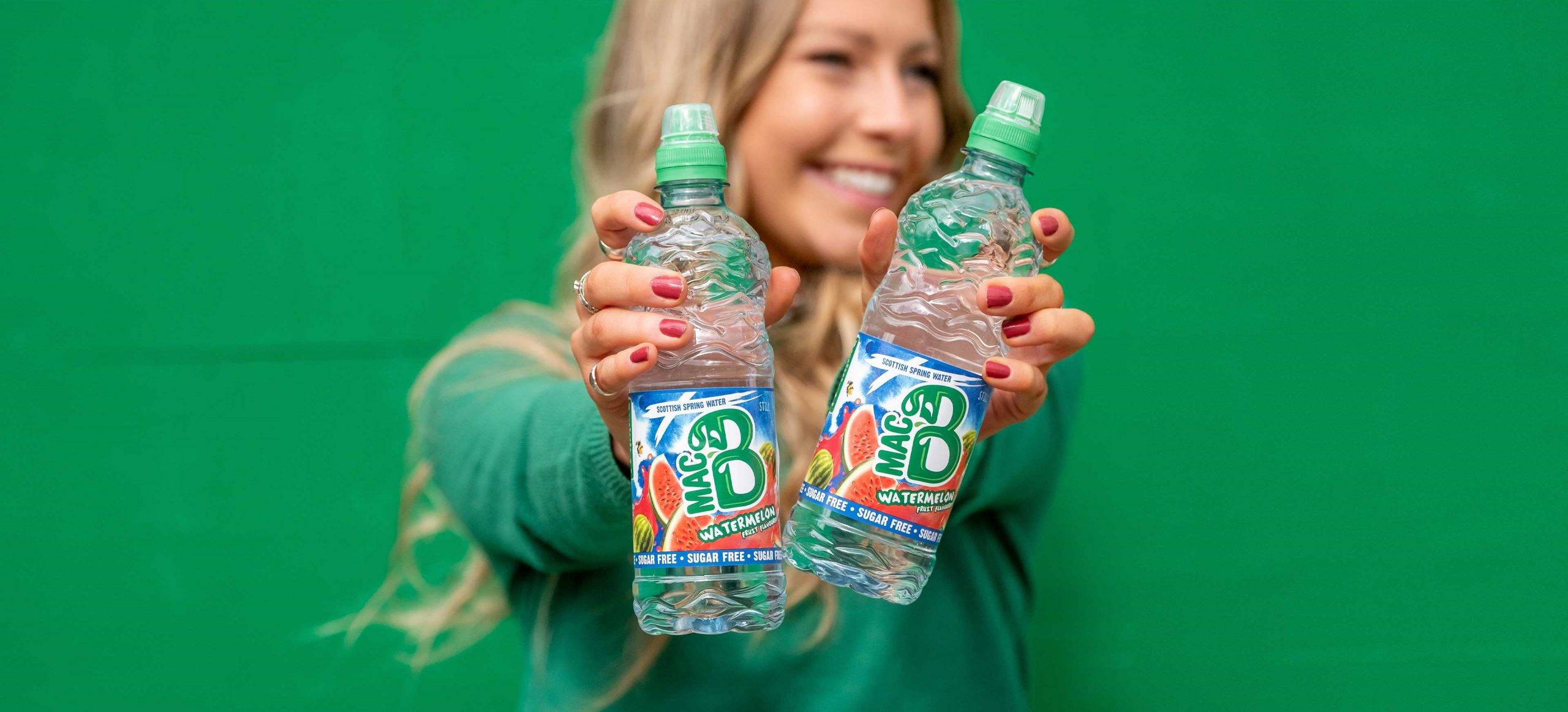 A woman holding two bottles of Macb Watermelon flavoured spring water